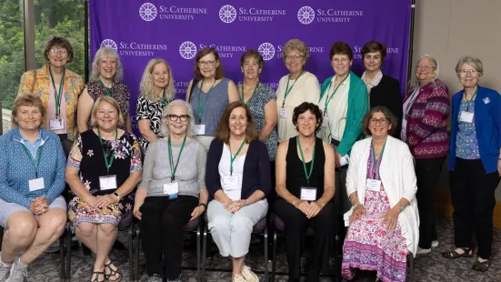 Two rows of women, the front row sitting, the back row standing, pose in front of a purple backdrop.