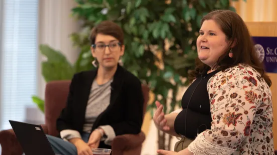 One book club host gestures while talking; another listens in the background.