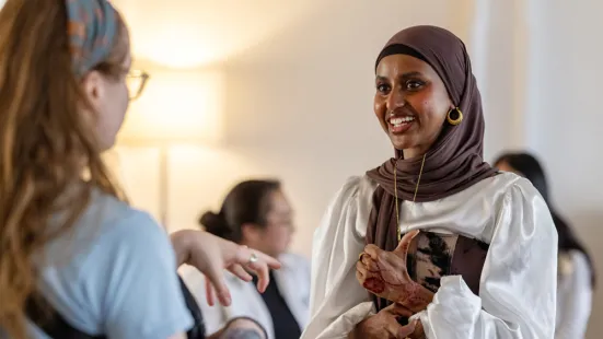 A woman smiles while talking to someone whose back is to the camera.