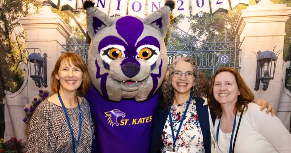 Three women wearing lanyards pose with the Katie Cat mascot.