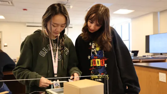 Two students in a classroom look down at a tablet on a table.