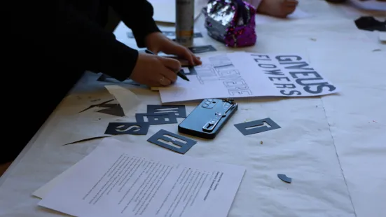 A pair of hands rest on a poster with hand-lettering; other papers and stencils are scattered on the table as well.