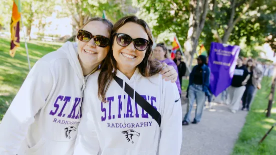 Two students wearing sunglasses and sweatshirts smile outside.