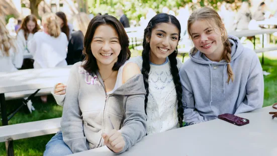 Three students sitting a picnic table smile.