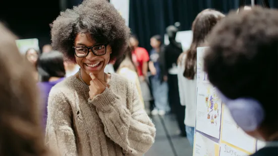 A student smiling in front of a poster at someone out of frame. In the background are different posters and presenters.