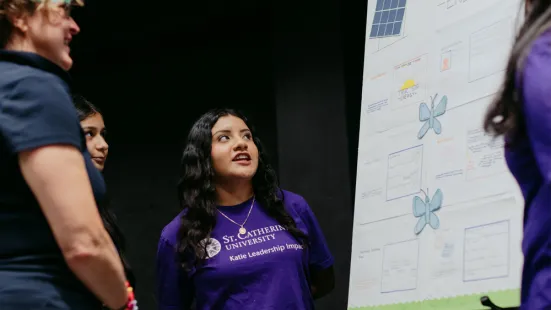 A student in a purple St. Kate's shirt talking about a poster to her left.
