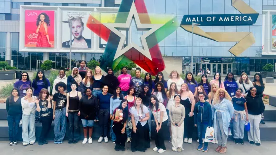 A large group of students standing in front of the sign for the Mall of America.