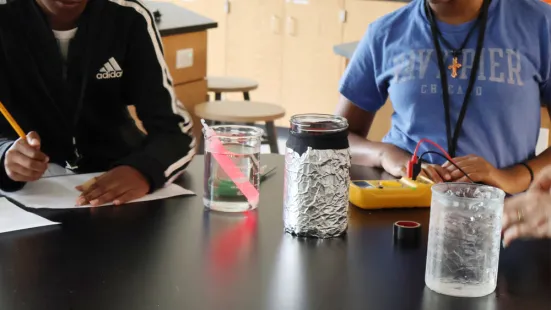 A close up of a glowstick in water with two students recording information on its temperature.
