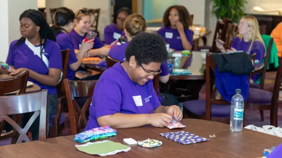 Students wearing purple St. Kate's shirts hand-stitching fabric at a table during a campus activity.