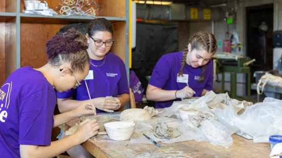 Students working with clay at a shared table in an art studio, wearing purple St. Kate's shirts.
