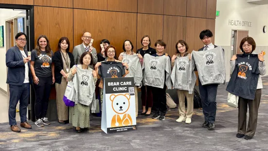 A group of smiling people stand and hold up gray T-shirts.