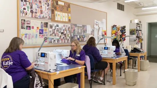 At two tables, people sit and work on sewing machines.