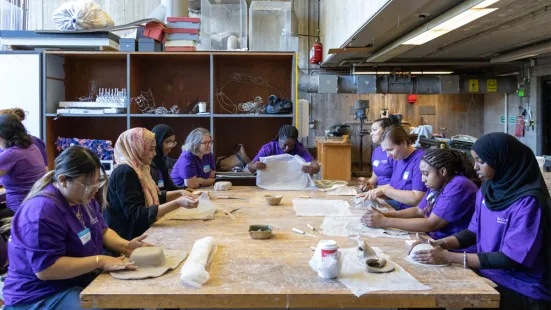 People sit around a wooden table and mold clay with their hands.