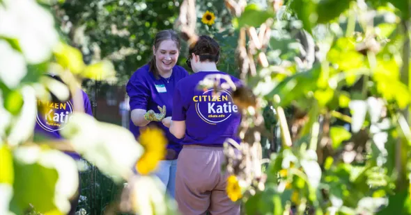 Two people wearing purple laugh together, framed by out-of-focus greenery.