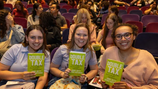 Three audience members smile and each hold up a copy of Opoku-Agyeman's book, The Double Tax.
