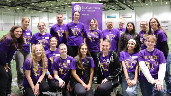 A group of St. Kate's students, faculty, and staff pose in a gym.