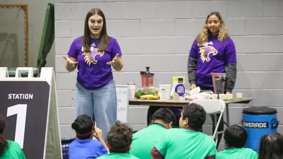 A student gestures while teaching a group of sitting children.