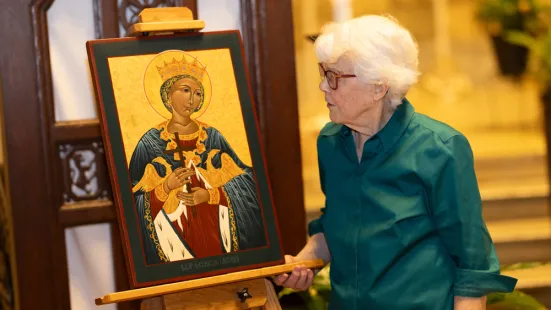 A white-haired woman looks at an icon of Saint Catherine on an easel. 