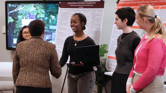Mayor Her shakes the hand of a student, standing in front of research posters.