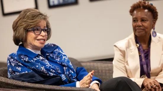 Valerie Jarrett talks in the foreground while President Evans listens in the background.