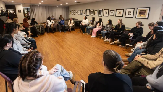 A group of people are seated in a large circle of chairs.