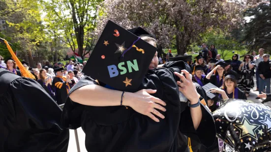 A graduate wearing a cap with letters that say "BSN" receives a hug.