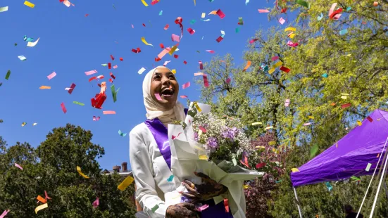 Colorful confetti falls down around a smiling graduate holding a bouquet of flowers.