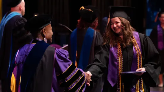 A graduate shakes hands with President Evans after receiving her diploma on stage.