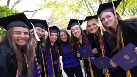 A group of graduates in caps and gowns lean in and smile.