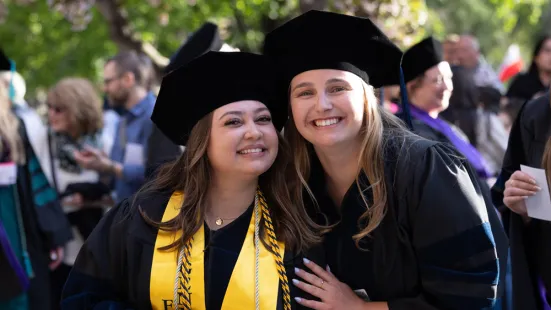Two graduates smile outside ahead of Commencement.