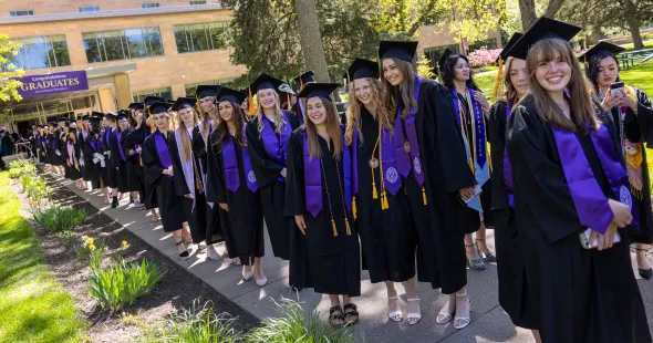 Graduates in caps and gowns line up outside for Commencement.