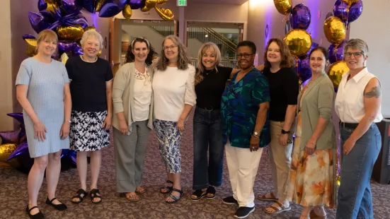A group of alumni pose in front of purple and gold balloons at Reunion.