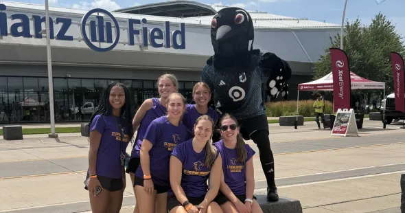 Wildcat soccer team members pose in front of Allianz Field with the loon mascot.