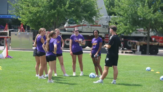 Wildcat soccer players stand in a circle on a soccer field during the STEM clinic.