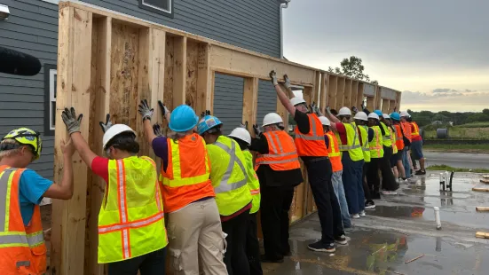 Volunteers in neon safety vests raise up a wooden wall frame.
