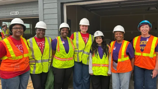 St. Kate's volunteers wearing neon safety vests and hard hats pose and smile. 