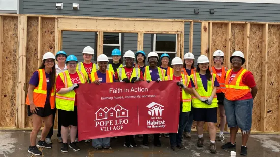 A group of people wearing neon safety vests and hard hats pose with a red banner.