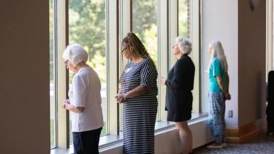 Four women stand looking outside a window.