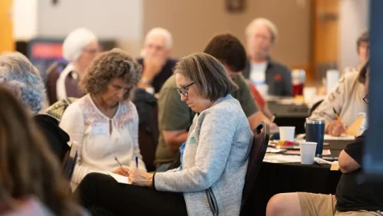 People sit at a table, each writing in a notebook. 