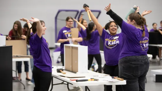 Volunteers in purple shirts celebrate while building dressers for Citizen Katie.