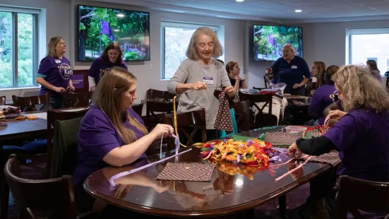Volunteers sit at at table and weave together colorful ribbons. 