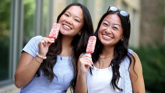 Two students smile while holding popsicles