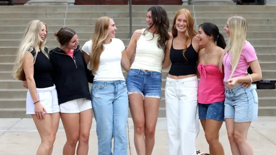 A group of students laugh and pose outside with their arms around each other. 