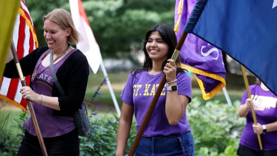 A woman in a purple shirt smiles while holding a flag.