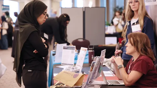 A student, standing, talks to an employer sitting at a table.