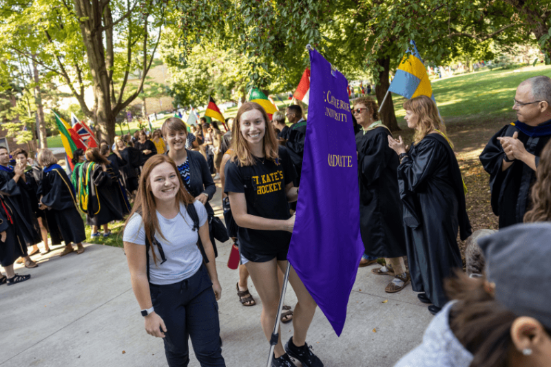 Two people walk with a purple banner that reads "Graduate"