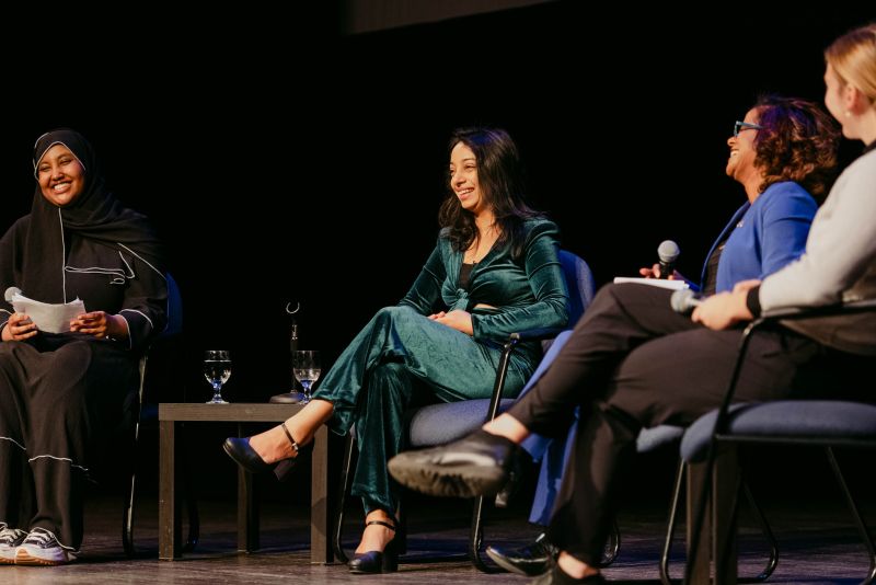 A panel of four women sit on stage and talk. 