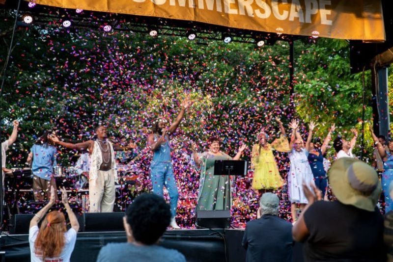 black musicians on stage celebrating. they are surrounded by confetti. people in the audience are clapping