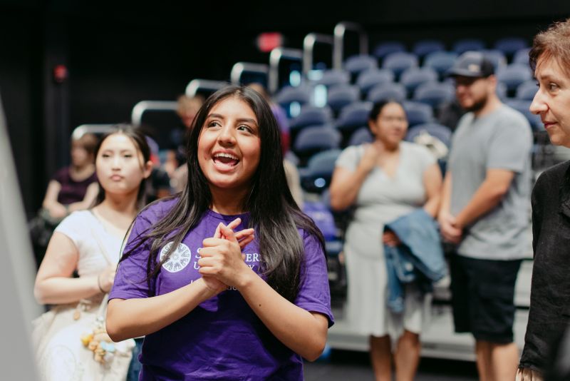 A student wearing a purple St. Kate's shirt looking at and talking about an out of frame poster presentation.