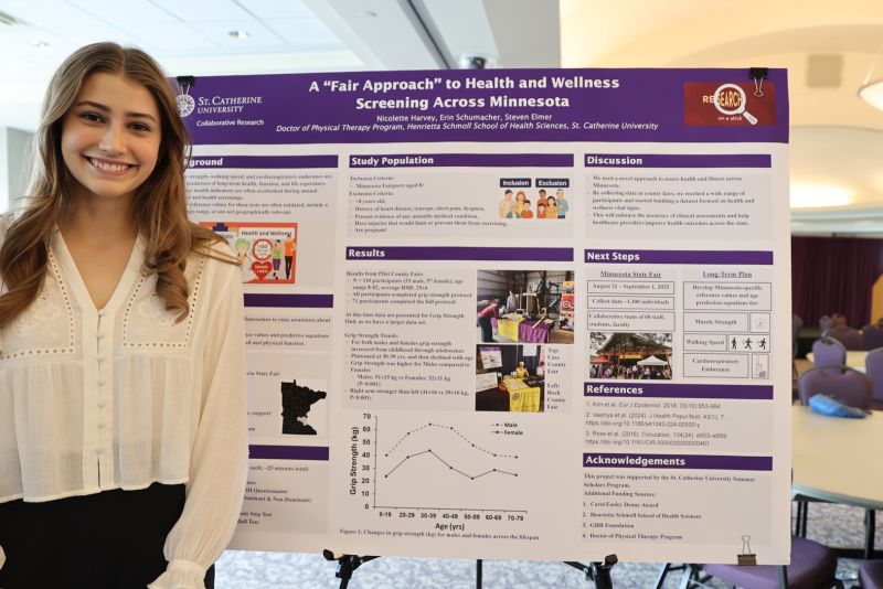 A student with long blonde hair smiles and stands in front of a poster board with research.